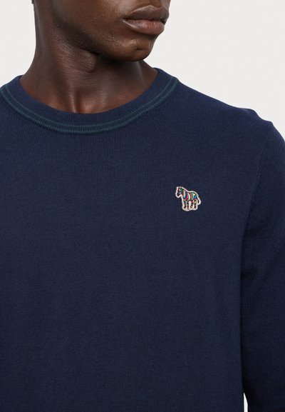Navy knit sweater with green ribbed neckline, featuring a small multicolored horse logo on the chest. Soft texture, slim fit design.