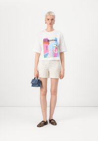 White short-sleeve t-shirt with colorful Havana graphic, paired with textured cream shorts, holding a blue handbag, wearing leopard print shoes.