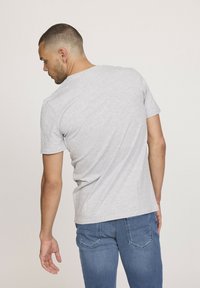T-shirt gris à manches courtes avec un col rond, fabriqué en coton léger. Porté avec un jean bleu, montrant une coupe décontractée vue de dos.
