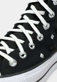 Μαύρα καμβά παπούτσια μέσης με λευκές κορδόνες, ασημένιες θηλιές, και διακοσμητικές σούστες και φιόγκους. Λευκή καουτσούκ σόλα με υφή.