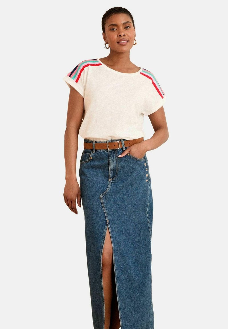 Balta marškinėliai su spalvingomis petnešomis, derinami su aukštu juosmeniu džinsine sijonu, turinčiu priekinę skeltą ir mygtukų detalizaciją.