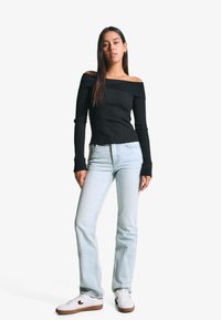 Black ribbed off-the-shoulder top with long sleeves, paired with light blue straight-leg jeans and white sneakers with brown soles.