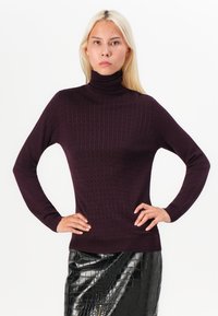 Burgundy ribbed turtleneck sweater with long sleeves, featuring a fitted design and textured pattern, paired with a black glossy faux leather skirt.