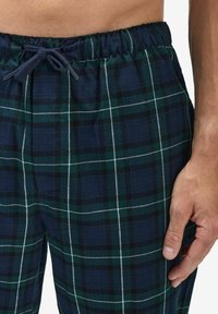 Klassiset ruudulliset pyjama-housut, joissa on joustava vyötärö. Värityksessä tummansinisiä, vihreitä ja valkoisia viivoja. Kevyt, pehmeä materiaali, joka on hyvin löysä.