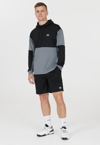 Lätt grå och svart hoodie med framfickor, tillsammans med svarta shorts. Har logotyp och en avslappnad sportdesign.