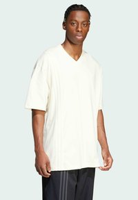 Light beige v-neck t-shirt in soft fabric, featuring short sleeves and subtle vertical seams on the front. Worn with dark shorts.