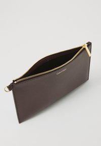 Bordo kožni clutch s zatvaračem na zip, zlatnim hardverom i reljefnim logom. Glatka vanjština, tanka silueta i obložena unutrašnjost.