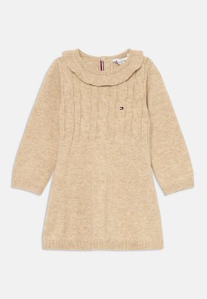 Μπεζ πλεκτή φόρεμα με σχέδιο καλωδίωσης, ριγωτό γιακά και μανσέτες, μακριά μανίκια και λογότυπο στο στήθος. Απαλή υφή και χαλαρή εφαρμογή.