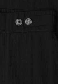 Gros plan sur un tissu noir avec deux boutons ronds gris sur une ceinture comportant des passants cousus et un élastique froncé.