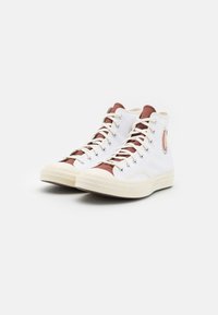 Wysokie sneakersy z białej kanwy, brązowymi akcentami i off-white gumowymi podeszwami; posiadają kontrastowe sznurowadła i oczka.