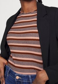 Brun og pink stribet top med et tekstureret, ribbet mønster og en bølget halsudskæring, lagt under en sort blazer. Blå jeans med en knapdetalje.