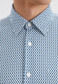 Button-up shirt featuring a blue and white geometric pattern, cotton fabric, a spread collar, and white buttons. Small chest pocket included.