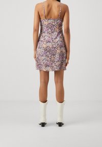 Šaty bez rukávů s květinovým vzorem, se vypasovaným trupem a rozšířenou sukní, vyrobené z lehkého materiálu. Kombinované s bílými kotníkovými botami.