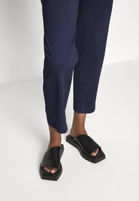 Sandales à enfiler en cuir noir avec un bout ouvert, dotées d'une large bride sur le pied et d'une semelle rectangulaire épaisse.