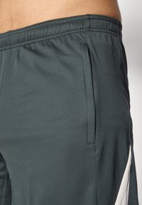 Dark green athletic shorts made of textured fabric. Features an elastic waistband and contrasting white side panel.