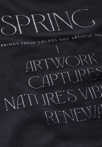 Tissu noir avec un texte en relief blanc indiquant "LE PRINTEMPS APPORTE DES COULEURS FRAÎCHES ET UNE PERSPECTIVE ARTISTIQUE | L'ŒUVRE CAPTURE LE RENOUVEAU VIBRANT DE LA NATURE."