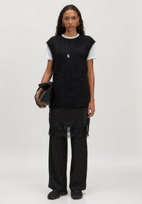 Black knit oversized vest over a white t-shirt, paired with a sheer black layered skirt featuring lace trim and wide black pants.