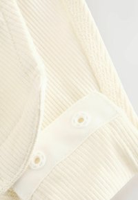 White ribbed fabric with a smooth collar edge and a tab featuring two white buttonholes. Textured surface with accent stitching visible.