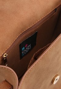 Interior de bolso de ante beige con un bolsillo con cremallera. Presenta herrajes dorados y una etiqueta negra con un logo de colores. Textura suave, diseño minimalista.