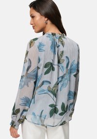 Floral-patterned blouse in lightweight fabric; features blue flowers and green leaves on a white and striped background. Long sleeves with gathered cuffs.