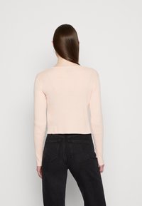 Heledad roosa ribidega pikkade varrukatega topp, millel on ümar kaelus ja lühike ääreline, koos mustade teksadega, millel on kaks tagataskut.