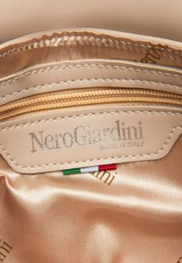 Beżowe skórzane wnętrze z z�łotym zamkiem błyskawicznym i jedwabistą teksturą. Zawiera logo "NeroGiardini", napis "MADE IN ITALY" oraz detale flagi włoskiej.