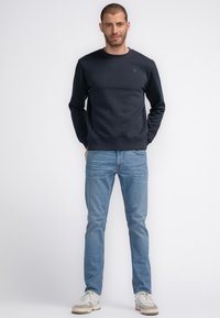 Marineblauwe sweatshirt met ronde hals, zachte textuur en ribgebreide manchetten, gecombineerd met lichtblauwe rechte jeans en casual sneakers.