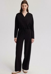 Mono negro con frente cruzado, mangas largas y cintura con cordón. Presenta pantalones de pierna ancha y una textura suave y lisa.