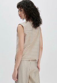 Beige mouwloos topje met verticale marineblauwe strepen, met een ronde halslijn en een losse pasvorm. Hete soepele textuur en subtiele details aan de achterkant.