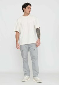 T-shirt crema a maniche corte con scollatura rotonda, abbinata a pantaloni cargo grigi chiari con tasche laterali e dettagli di cucitura sottili.