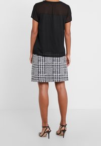 Top negro con panel de tela transparente, combinado con una falda de cuadros en blanco y negro. Los tacones tienen tiras delgadas y un diseño de punta.