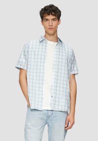 Korte mouwen overhemd in lichtblauw met een ruitpatroon. Witte T-shirt met ronde hals eronder. Gemaakt met lichtblauwe jeans.