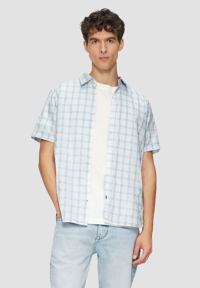 Korte mouwen overhemd in lichtblauw met een ruitpatroon. Witte T-shirt met ronde hals eronder. Gemaakt met lichtblauwe jeans.