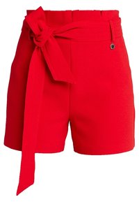 Vysoké červené kraťasy s širokým látkovým opaskem uvázaným do mašle v pase a malým kovovým přívěskem na pásku.