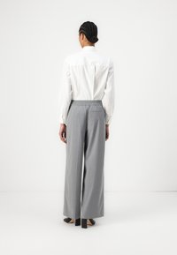 Grå vide benbukser med elastisk talje, parret med en hvid skjorte med knapper. Outfittet har rene linjer og minimal design.