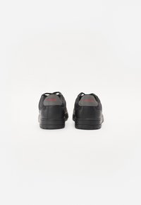 Czarne sneakersy o gładkim skórzanym wykończeniu i gumowych podeszwach. Zawierają czerwone logo "HUGO" na pięcie oraz zaokrąglony kształt noska.