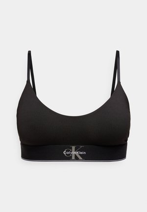 Melns Calvin Klein bralets ar plānām siksniņām un zīmola elastīgu joslu zem krūtīm uz vienkārša balta fona.