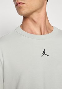 Lyst lys grå bomulds sweatshirt med rund halsudskæring og et lille sort Jumpman-logo broderet på brystet. Glat tekstur.