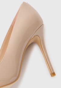 Nude patent leather high heel shoe with a pointed toe and a slim stiletto heel, featuring a smooth glossy finish and minimalistic design.