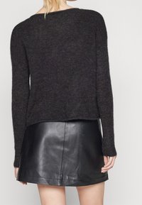 Svart stickad tröja med långa ärmar och en avslappnad passform, kombinerad med en skinande svart läderkjol i mini-längd, med en rak nederkant.