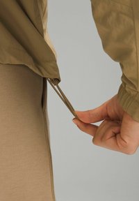 Serrage à la main d'un cordon de serrage réglable sur l'ourlet d'une veste beige claire, sur un pantalon beige, sur un fond neutre.