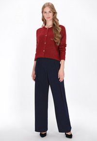 Rode gemêleerde cardigan met ronde hals en knoopsluiting, gecombineerd met marineblauwe wijde broek en zwarte hoge hakken.