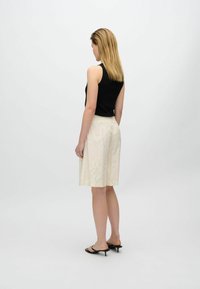 Black ribbed tank top paired with a cream-colored skirt featuring a subtle floral pattern, ankle-length with an elastic waistband, and black heeled sandals.
