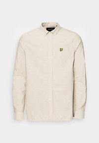 Kermanbutton-up-paita, joka on valmistettu teksturoidusta kankaasta, pitkät hihnat, rintatasku ja pieni keltainen brodeeraus vasemmalla puolella.
