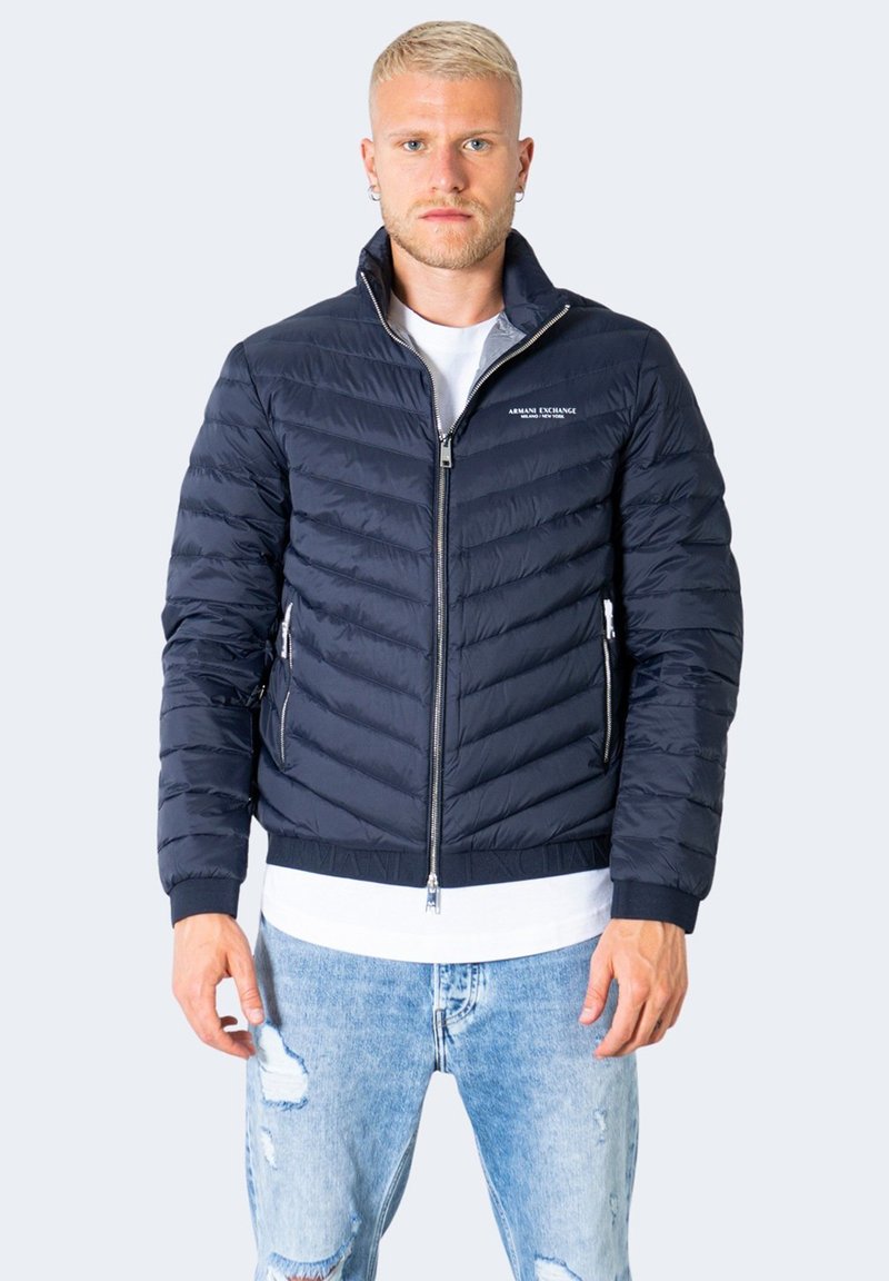 Giacca puffer navy con design trapuntato, chiusura con zip, colletto rialzato e tasche laterali. Presenta logo sul petto e polsini a coste.