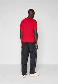 Rød t-skjorte med rund hals og korte ermer, kombinert med svarte lette joggebukser med hvit sidestripe og elastisk midje.