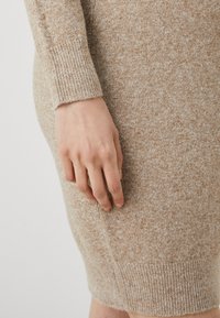 Abito maglione in beige mélange. Presenta polsini e orlo a coste, tessuto testurizzato con leggere variazioni e silhouette aderente.