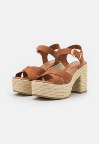 Sandali platform in suede marrone con cinturini incrociati, una fibbia regolabile e un tacco in juta intrecciata. La superficie strutturata aggiunge interesse visivo.