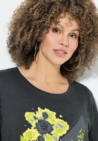 Zwarte shirt met een kleurrijk bloemontwerp in geel en grijs, ronde halslijn en korte mouwen. Zachte textuur, casual pasvorm.