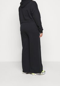 Czarna krótka bluza z kapturem, szerokie czarne spodnie dresowe oraz sportowe sneakersy z szarymi, białymi i neonowożółtymi akcentami.